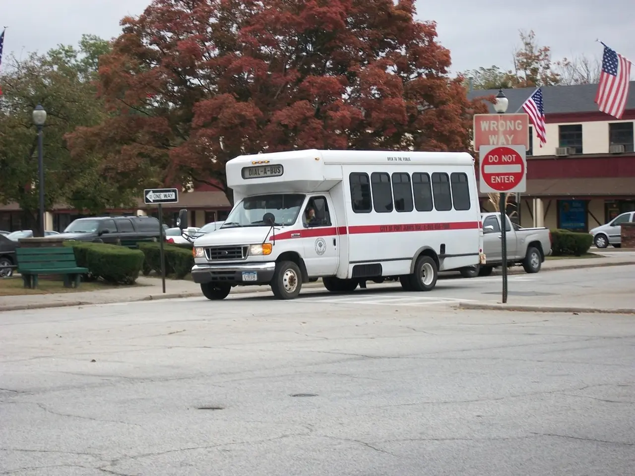 In this image I can see fleets of vehicles on the road, boards, plants, poles and benches. In the...