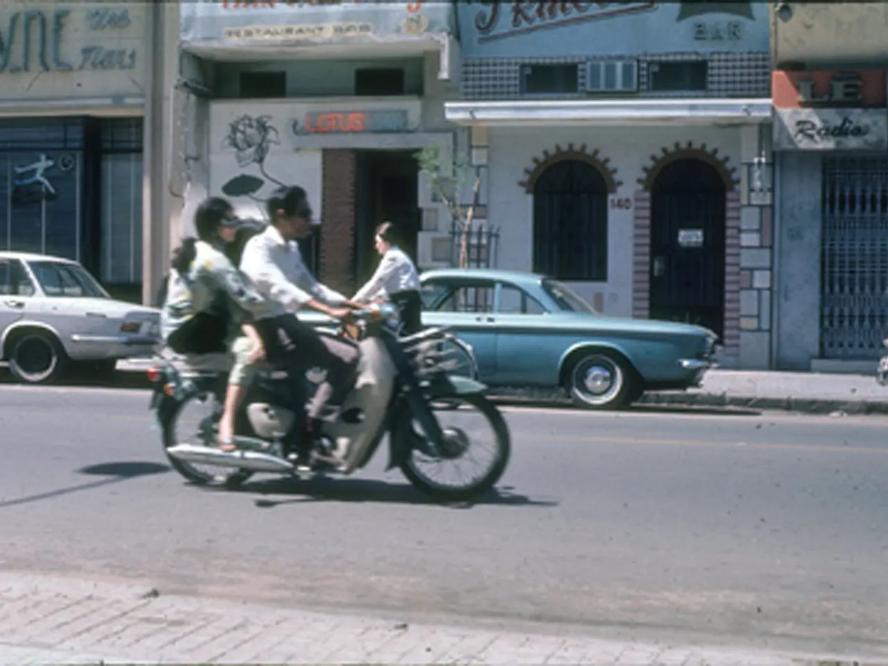 It is a road there is a footpath, to the left side on the road a man is riding a bike and two...