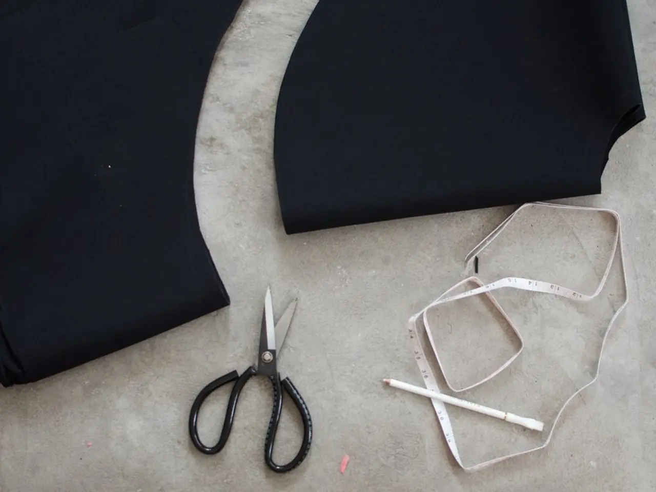 In this image we can see scissors, pencil, measuring tape and clothes on the floor.