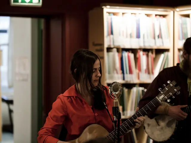In the image there is a lady and a man playing guitar in front of mic, the place seems to be inside...