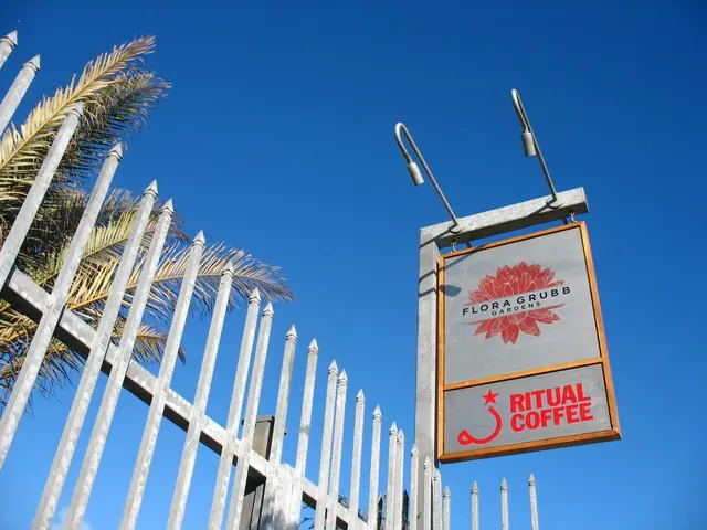 In this image we can see an advertisement board, street lights, grill, trees and sky in the...