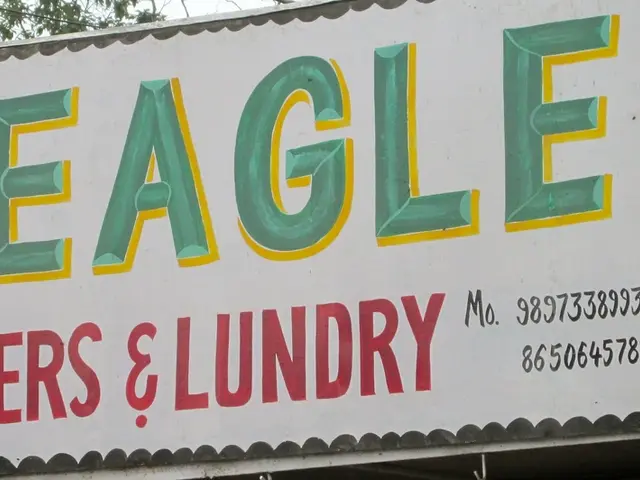 There is a hoarding on which eagle is written. Behind that there is tree and a wire.