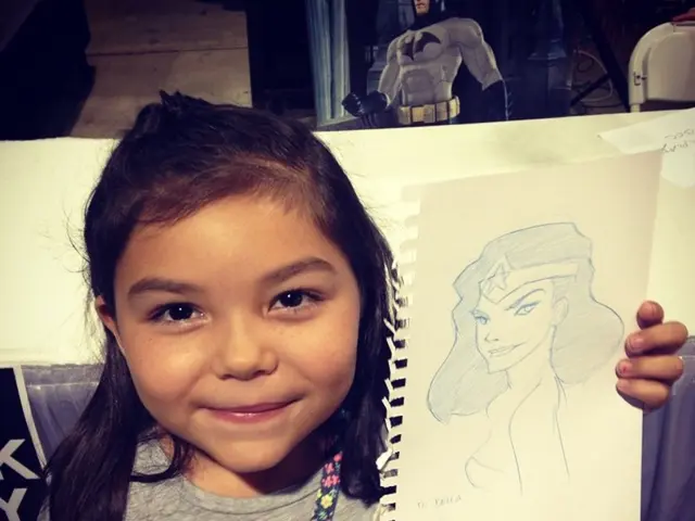 In this image we can see a girl is smiling, and holding a paper in the hand, and drawing on it.