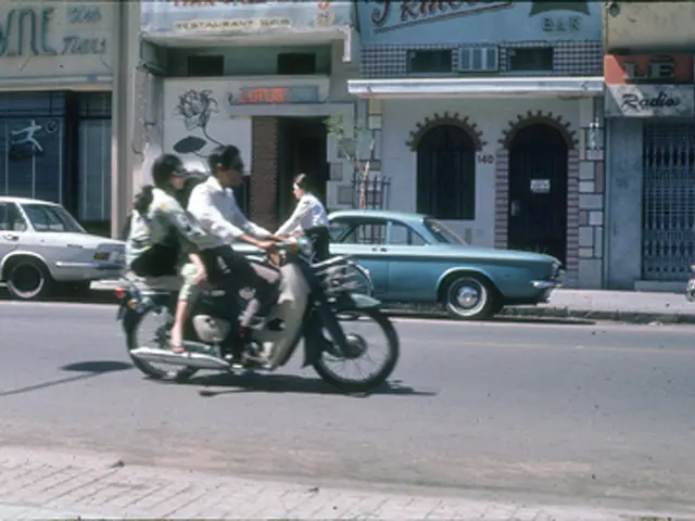 It is a road there is a footpath, to the left side on the road a man is riding a bike and two...