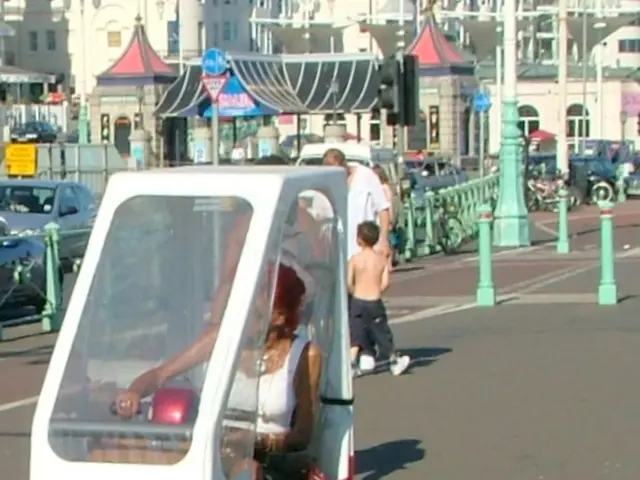 There is a person sitting in a vehicle and holding few belts which are attached to few dogs beside...