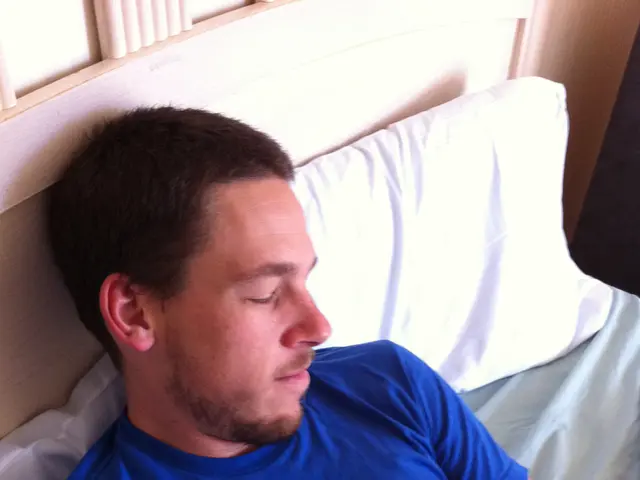 In this image we can see a man wearing blue shirt lying on a bed and holding a baby. We can also...