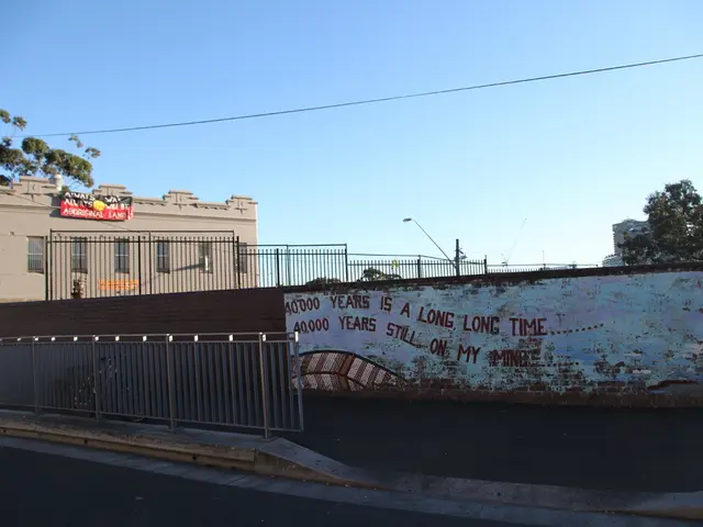 In the foreground of the picture there are road, railing, plant, wall, text and footpath. In the...